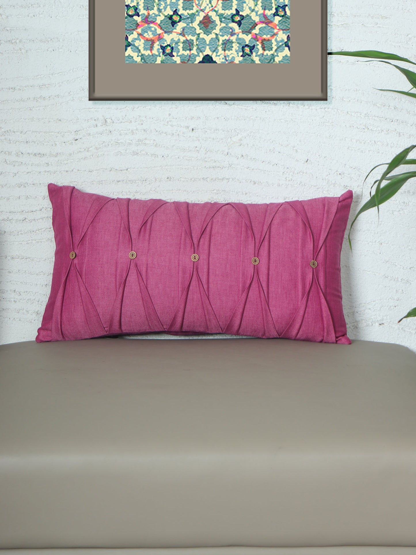 A rectangular magenta pink tufted lumbar pillow with five decorative brass buttons, resting on a beige leather sofa against a white textured wall.