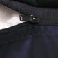 Close-up of a black zipper with a black pull tab on a dark navy or black fabric garment, showing a light-colored lining on one side.