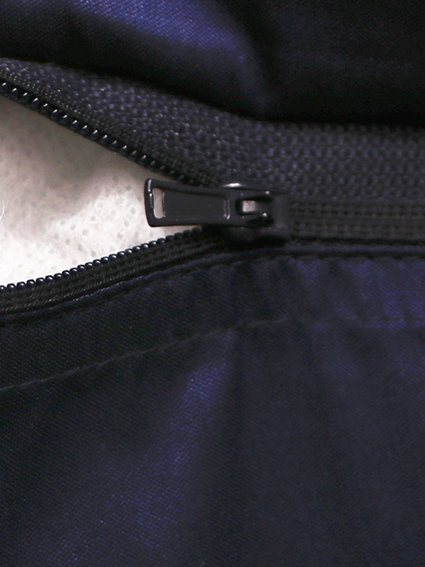 Close-up of a black zipper with a black pull tab on a dark navy or black fabric garment, showing a light-colored lining on one side.