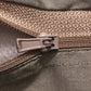 Close-up of a zipper pull in a muted taupe-brown color, showing the textured fabric and zipper teeth in detail.