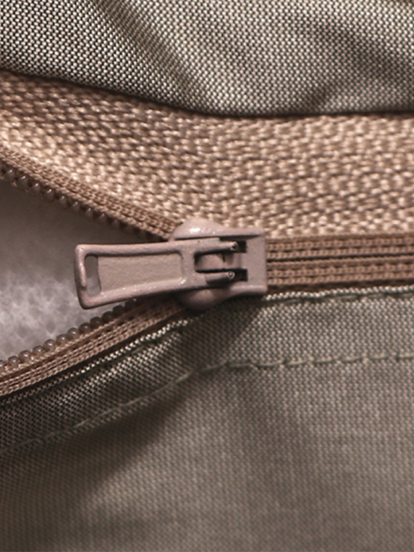 Close-up of a zipper pull in a muted taupe-brown color, showing the textured fabric and zipper teeth in detail.