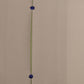 A minimalist wall art piece featuring a vertical olive green line with two small, round, dark blue metallic beads suspended at equal intervals, set against a plain beige wall.