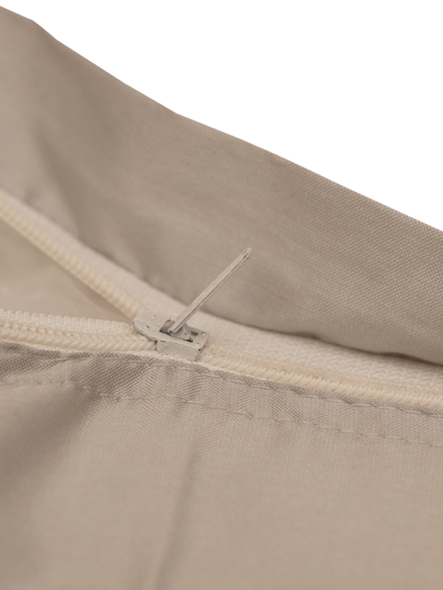 Close-up detail of a light beige fabric item with a cream zipper and a small metal pull tab, shown against a white background.