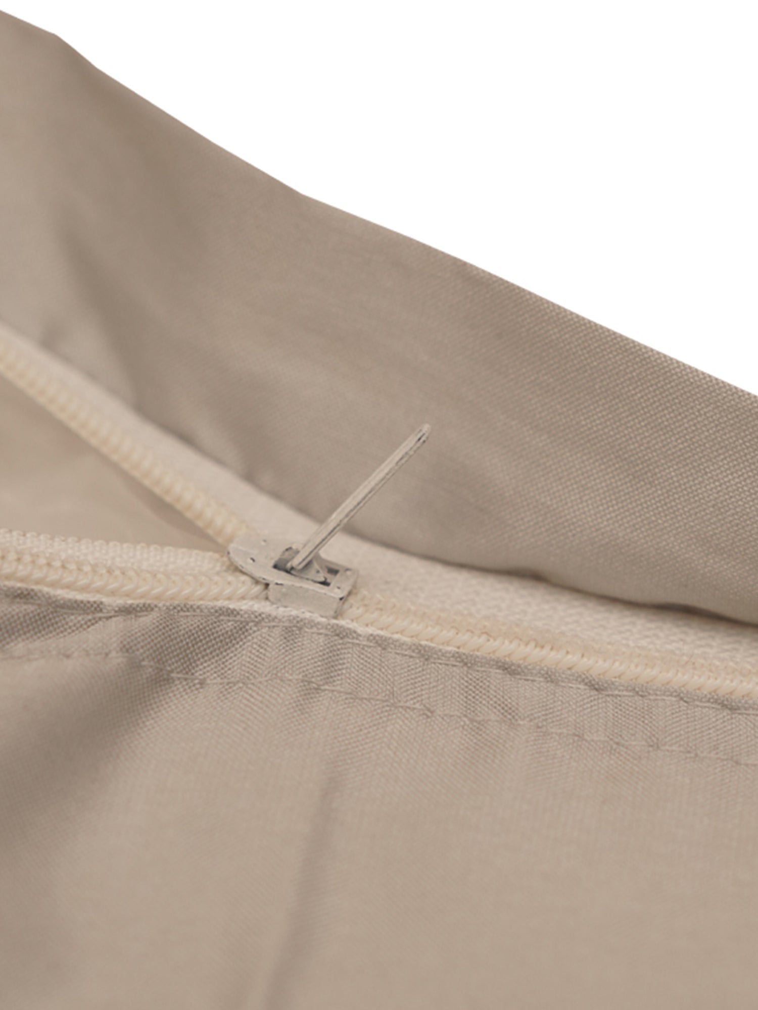 Close-up detail of a light beige fabric item with a cream zipper and a small metal pull tab, shown against a white background.