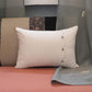 A square off-white throw pillow with three small gold decorative buttons on the right side, resting on a coral-pink sofa in front of a gray and beige patterned backdrop.
