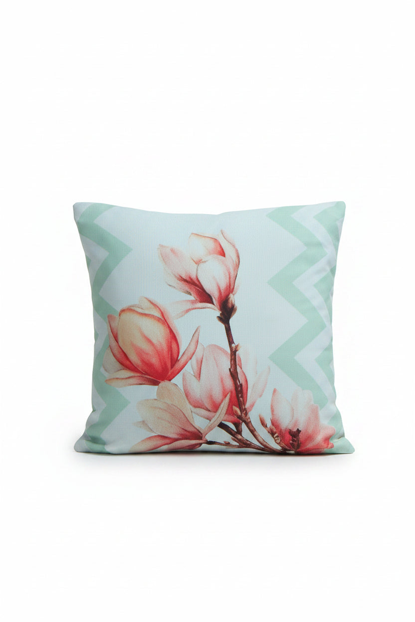 A decorative throw pillow with a pink floral print and mint green chevron border, styled on a blue wooden bench with a matching patterned white throw blanket.